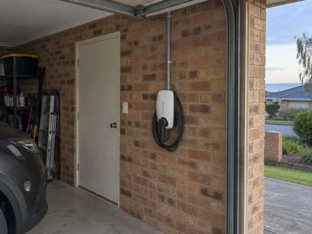 Wall-mounted EV charger on a brick garage wall beside a side door in a home garage in Noraville